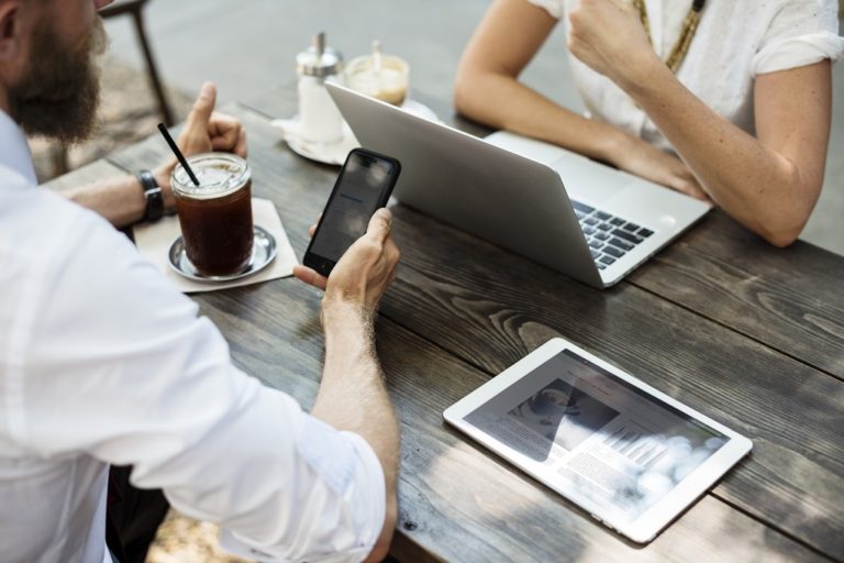 Two individuals at a table, focused on their laptops and phones, engaged in a productive work session.