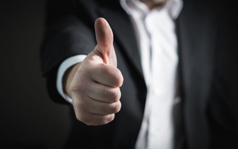 A man in formal attire showing a thumbs up gesture, representing encouragement and a positive attitude.