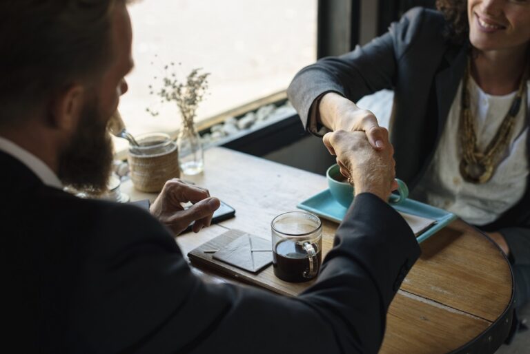 A man and woman shaking hands across a table, symbolizing agreement and collaboration in a professional setting.